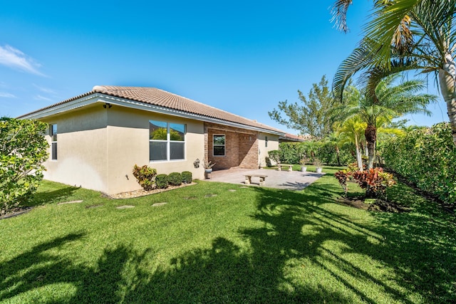 rear view of property with a tiled roof, a yard, a patio, and stucco siding