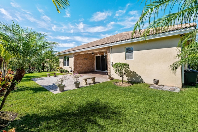 rear view of property featuring a patio, a tiled roof, a lawn, and stucco siding