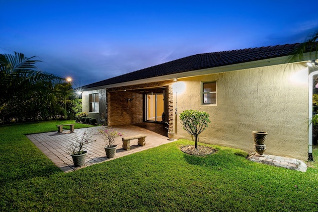 back of property at dusk featuring stucco siding, a yard, and a patio area