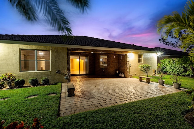 back of property at dusk featuring stucco siding, a patio, a yard, and ceiling fan