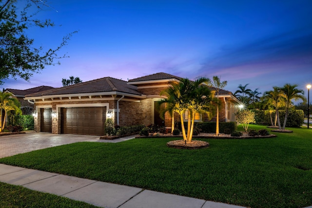 mediterranean / spanish house with a tiled roof, a front yard, decorative driveway, stone siding, and an attached garage