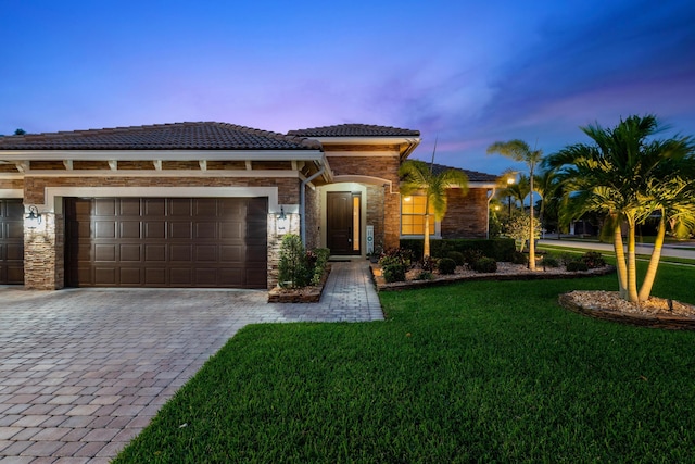 view of front of property featuring an attached garage, stone siding, a tiled roof, decorative driveway, and a lawn