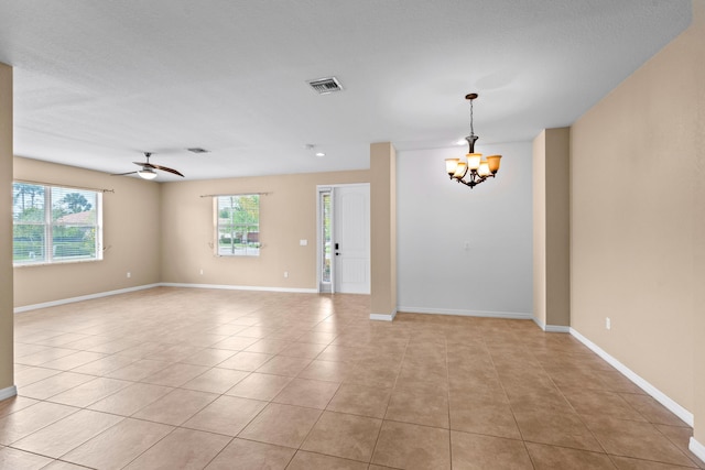 empty room with ceiling fan with notable chandelier, light tile patterned floors, a healthy amount of sunlight, and visible vents