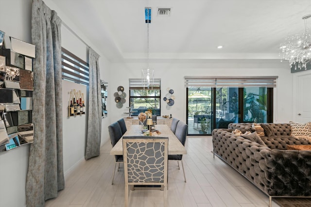 dining area with a tray ceiling, visible vents, light wood-style flooring, and an inviting chandelier