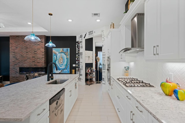 kitchen with visible vents, appliances with stainless steel finishes, white cabinetry, a sink, and wall chimney range hood