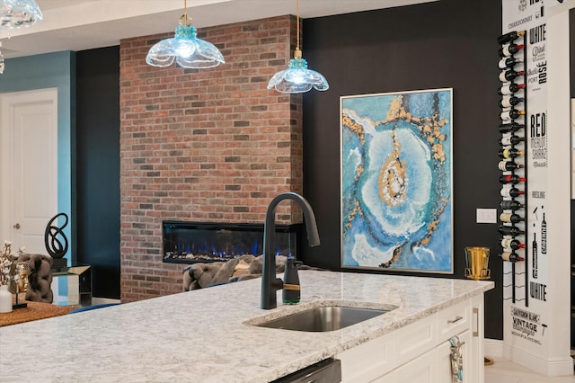 kitchen with hanging light fixtures, light stone countertops, a fireplace, white cabinetry, and a sink