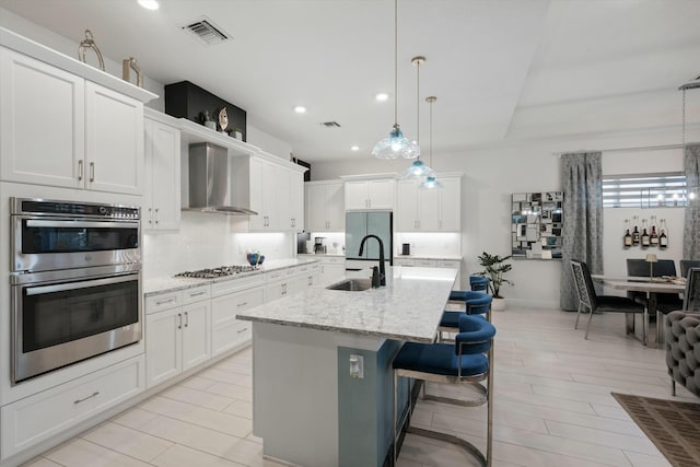 kitchen featuring stainless steel appliances, a sink, visible vents, wall chimney exhaust hood, and tasteful backsplash