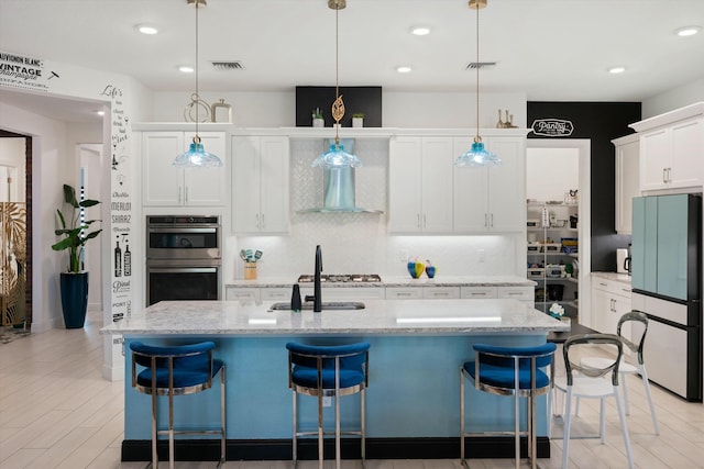 kitchen featuring stainless steel double oven, a breakfast bar area, visible vents, freestanding refrigerator, and tasteful backsplash