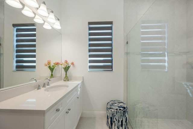 bathroom featuring tile patterned flooring, tiled shower, vanity, and baseboards