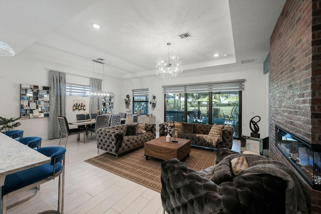 living area with an inviting chandelier, a fireplace, visible vents, and a raised ceiling