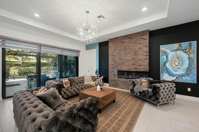 living room featuring a tray ceiling, a brick fireplace, visible vents, and an inviting chandelier