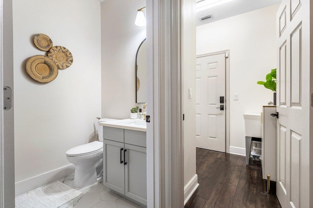 half bathroom with visible vents, toilet, wood finished floors, baseboards, and vanity