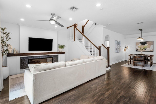 living area with arched walkways, visible vents, dark wood finished floors, and stairs