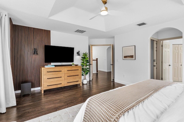 bedroom with arched walkways, visible vents, a tray ceiling, and wood finished floors