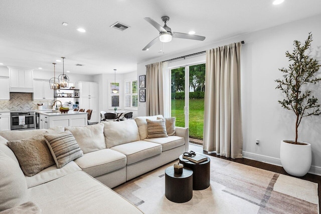 living room featuring visible vents, baseboards, light wood-type flooring, recessed lighting, and ceiling fan with notable chandelier