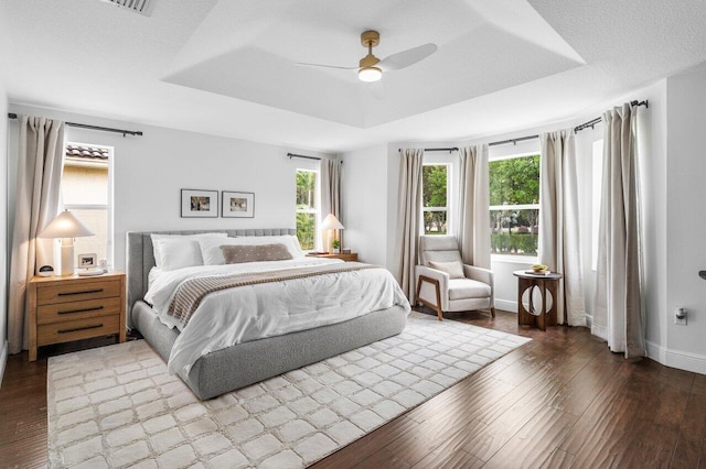 bedroom featuring a ceiling fan, wood finished floors, baseboards, a textured ceiling, and a raised ceiling