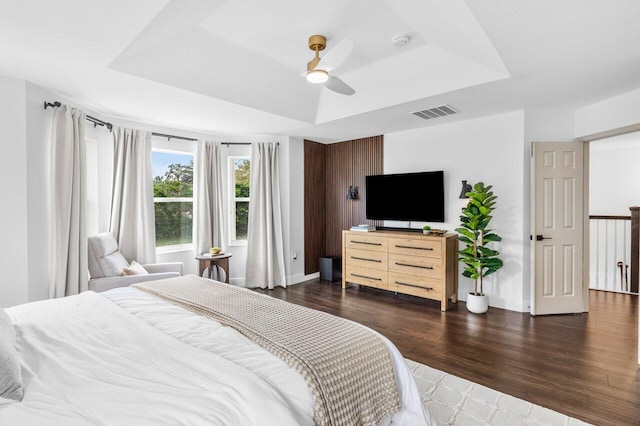 bedroom featuring a tray ceiling, visible vents, dark wood-style flooring, and baseboards