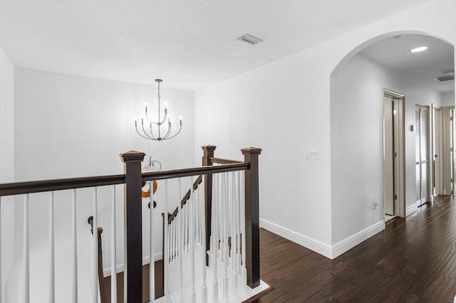 corridor featuring visible vents, an upstairs landing, wood finished floors, arched walkways, and baseboards