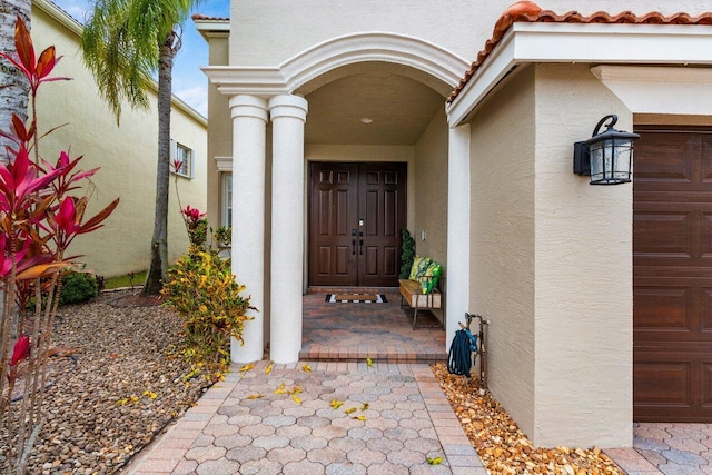 doorway to property with a tile roof, a garage, and stucco siding