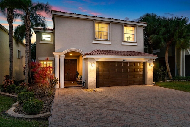 mediterranean / spanish home with stucco siding, a tiled roof, an attached garage, and decorative driveway