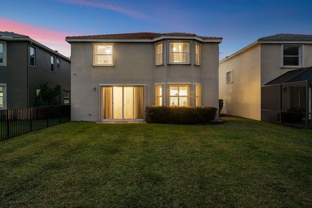 rear view of property featuring stucco siding, a lawn, a tile roof, and fence