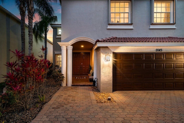 view of exterior entry featuring stucco siding, a garage, and a tiled roof