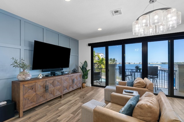 living area with a decorative wall, a notable chandelier, light wood-type flooring, and plenty of natural light