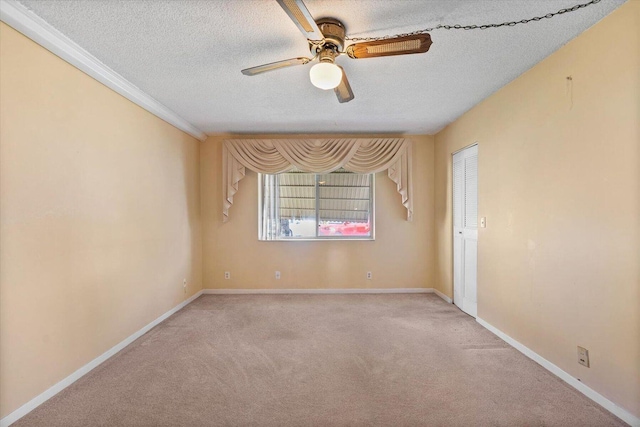 empty room with a textured ceiling, light colored carpet, a ceiling fan, baseboards, and crown molding