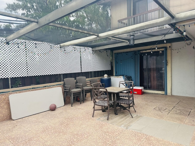 view of patio featuring outdoor dining space, a balcony, and glass enclosure