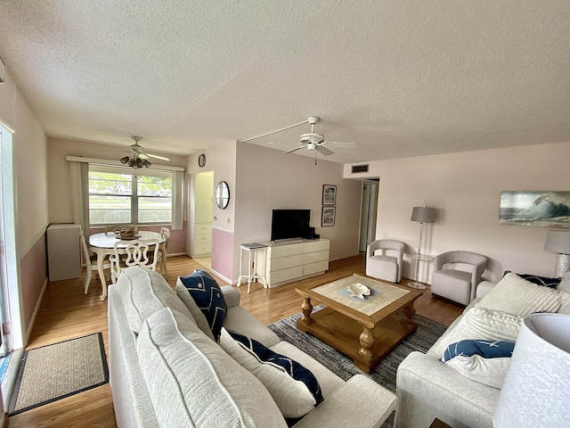 living room featuring a textured ceiling, light wood-type flooring, and a ceiling fan