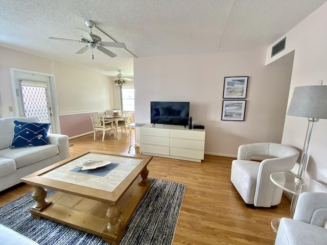 living area with light wood-style floors, visible vents, a textured ceiling, and a ceiling fan