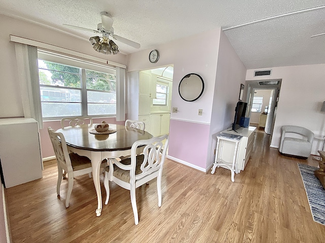 dining space with light wood finished floors, visible vents, baseboards, ceiling fan, and a textured ceiling