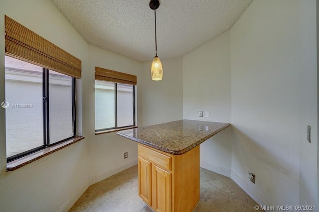 kitchen with a textured ceiling, baseboards, a peninsula, dark stone counters, and pendant lighting