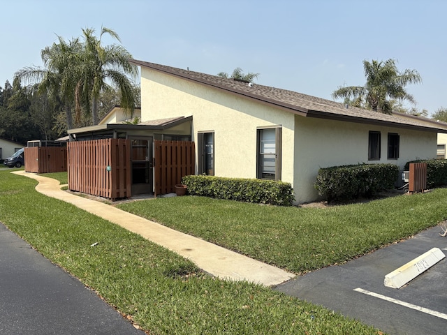 view of side of home featuring stucco siding, a lawn, roof with shingles, and fence