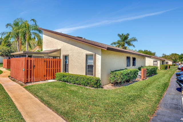 view of side of home with a gate, stucco siding, a lawn, and fence