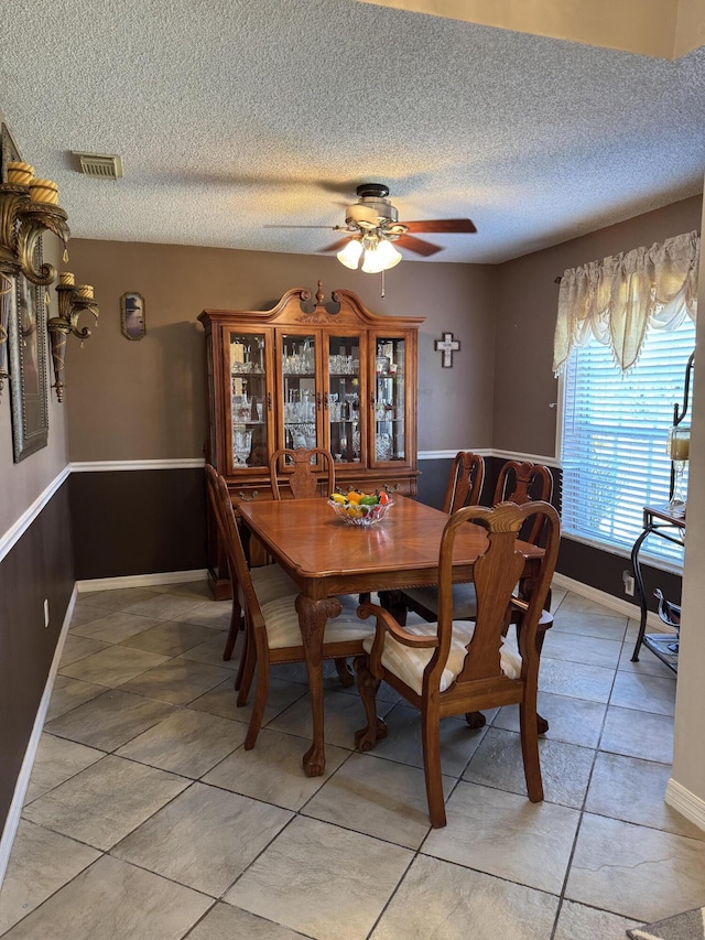 dining space featuring ceiling fan, visible vents, baseboards, and a textured ceiling