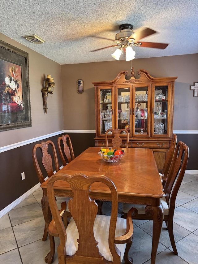 dining space featuring light tile patterned floors, baseboards, visible vents, a ceiling fan, and a textured ceiling