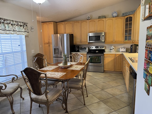 kitchen featuring lofted ceiling, light tile patterned flooring, light countertops, appliances with stainless steel finishes, and glass insert cabinets