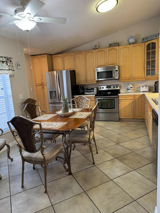 kitchen with stainless steel appliances, lofted ceiling, light countertops, glass insert cabinets, and light tile patterned flooring