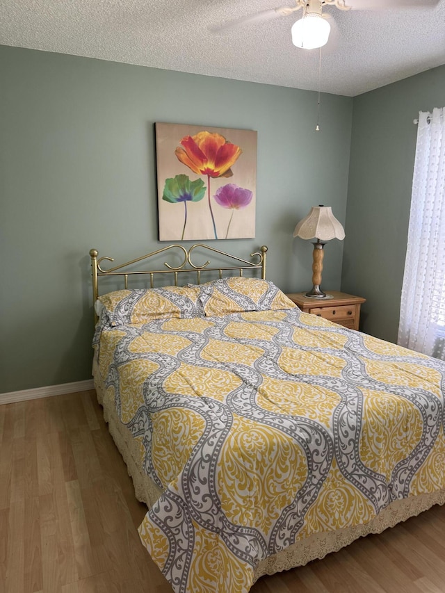 bedroom featuring a ceiling fan, a textured ceiling, baseboards, and wood finished floors