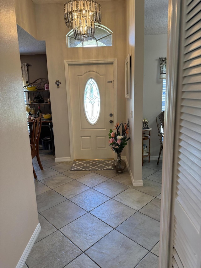 entrance foyer with a textured ceiling, light tile patterned floors, a notable chandelier, and baseboards