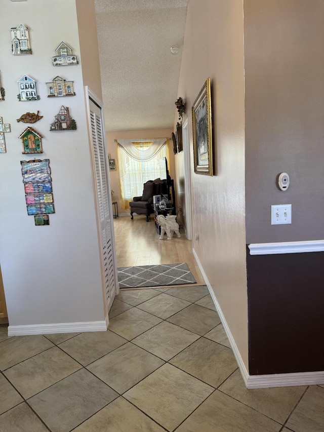 hallway with tile patterned flooring, baseboards, and a textured ceiling