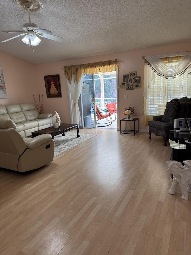 living room featuring ceiling fan, light wood-style flooring, and a textured ceiling