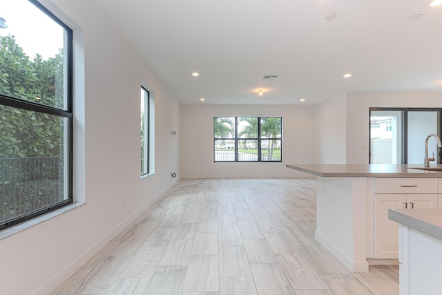 kitchen featuring baseboards, open floor plan, white cabinetry, a sink, and recessed lighting