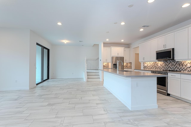 kitchen with a sink, white cabinetry, appliances with stainless steel finishes, tasteful backsplash, and a center island with sink