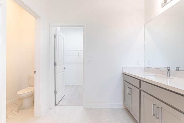 full bathroom featuring toilet, vanity, baseboards, marble finish floor, and a spacious closet