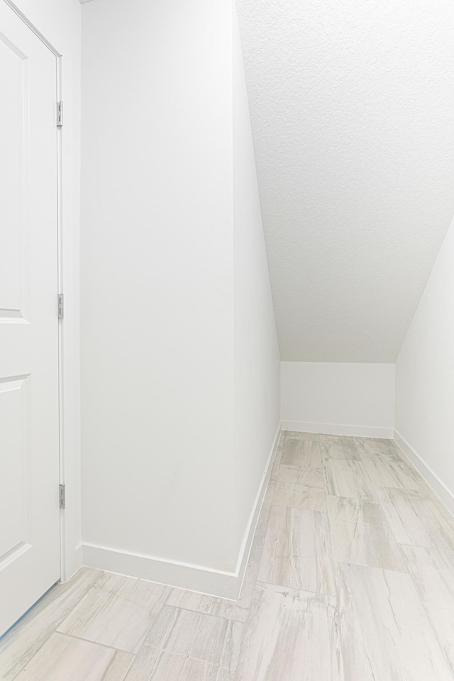 additional living space featuring lofted ceiling, a textured ceiling, and baseboards