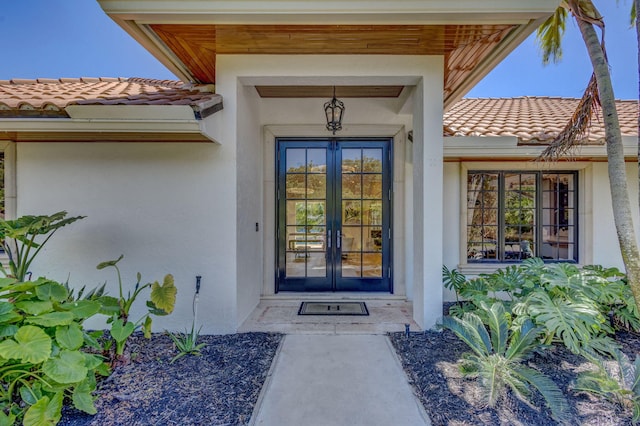 view of exterior entry featuring french doors, a tile roof, and stucco siding