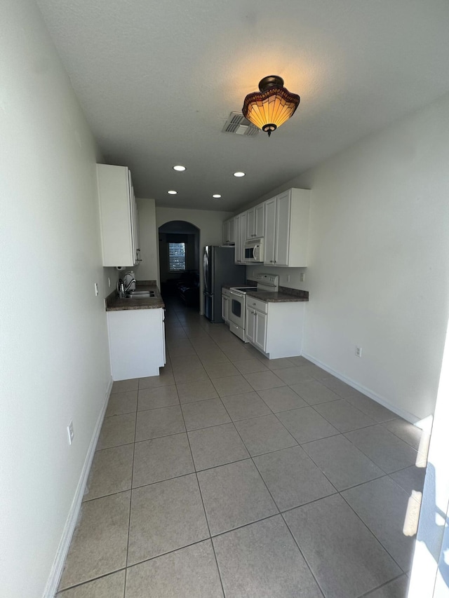 kitchen featuring white appliances, dark countertops, arched walkways, and a sink