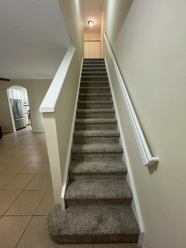 stairway with baseboards, arched walkways, and tile patterned flooring